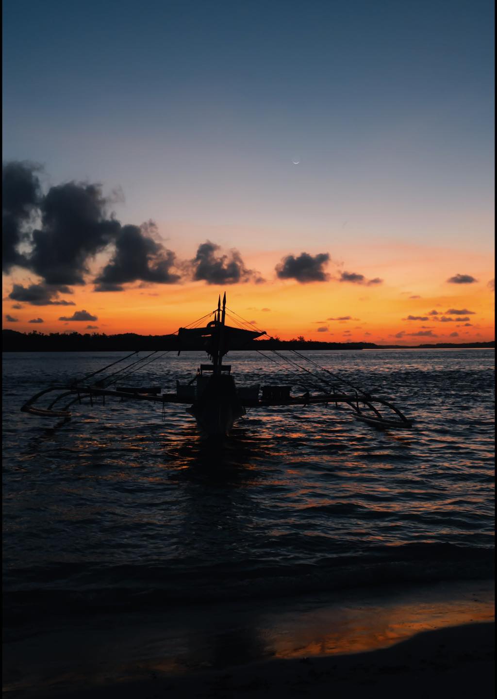 A wooden boat drifting across calm water at sunset